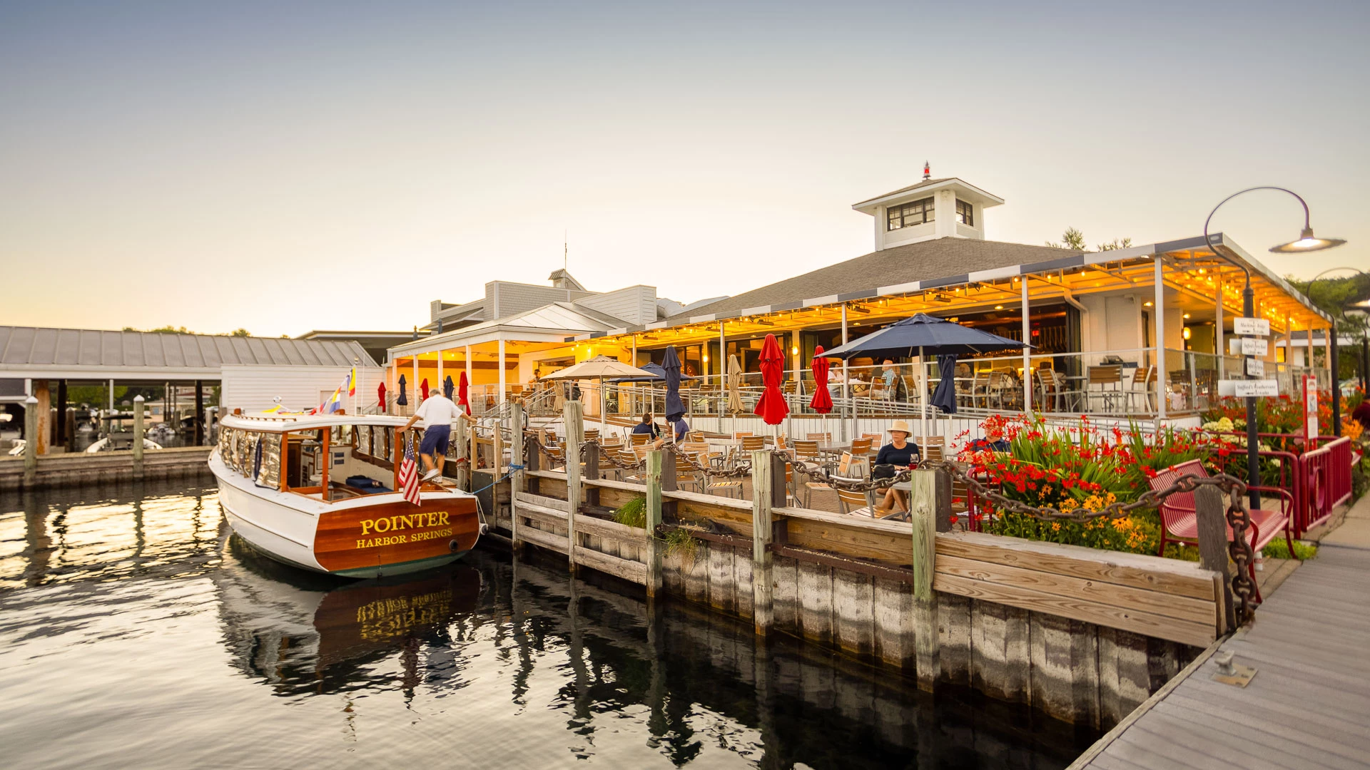 The Pointer boat docked at the restaurant's waterfront deck at dusk, string lights glowing over diners