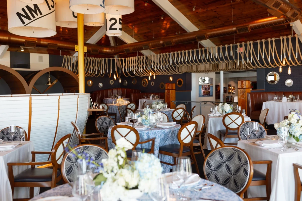 Dining room set for an event with blue-and-white linens, sailcloth pendant lights and rope-draped ceiling