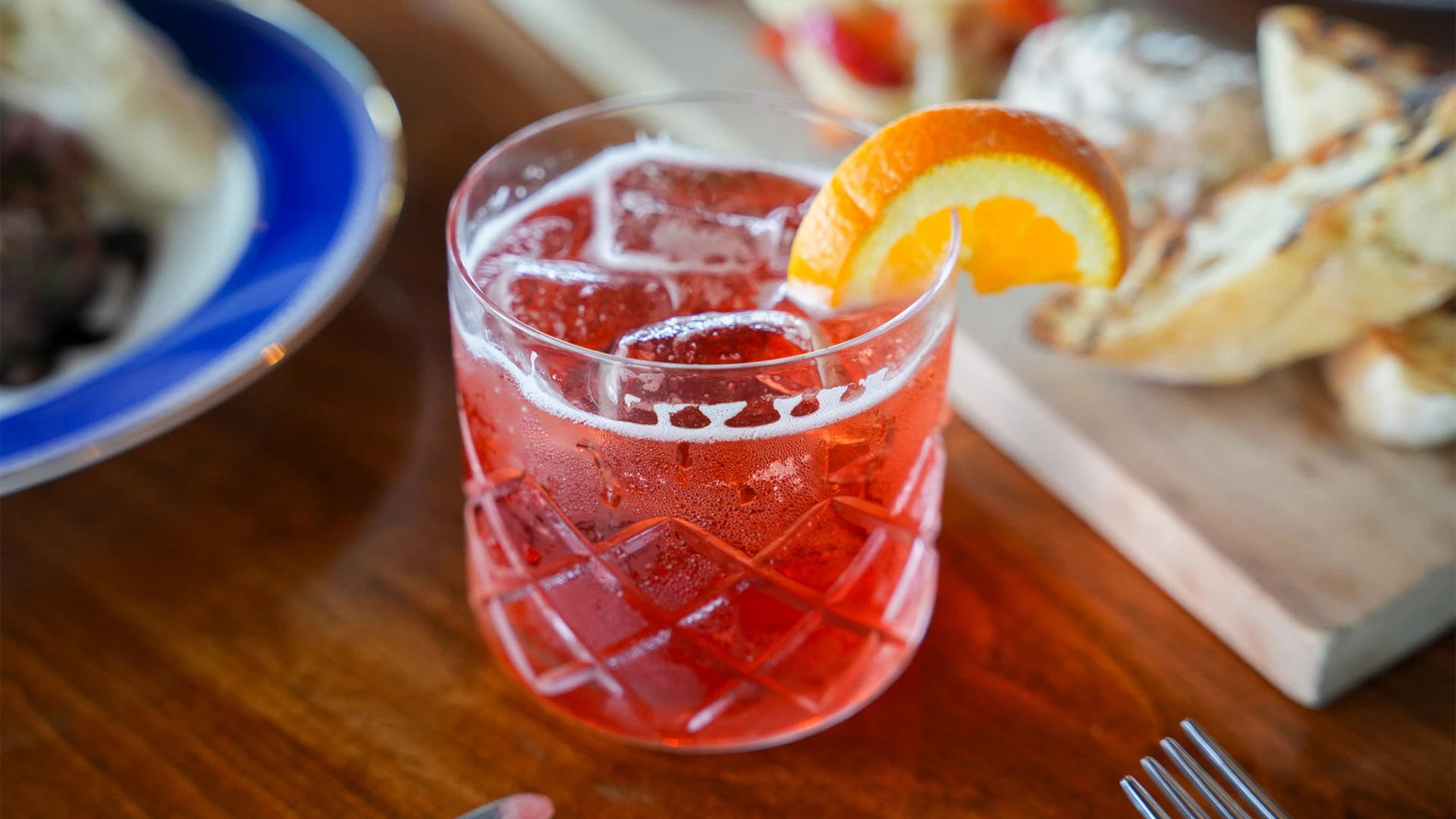 Cranberry-red cocktail garnished with an orange slice on a wooden table