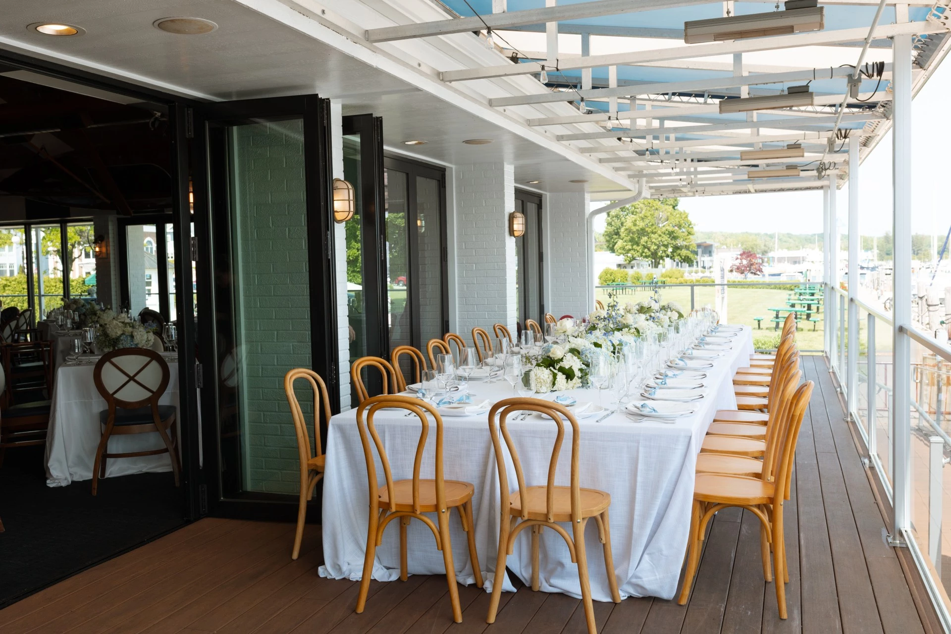 Long head table set with white linens and greenery on the covered waterfront deck