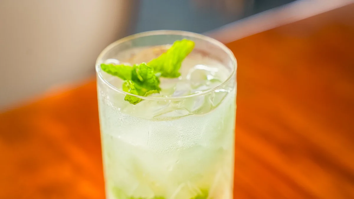 Tall glass of an iced mint cocktail on a wooden bar