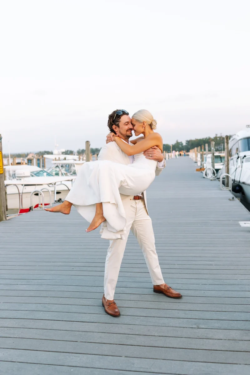 Groom lifting his bride in his arms on the marina dock at sunset