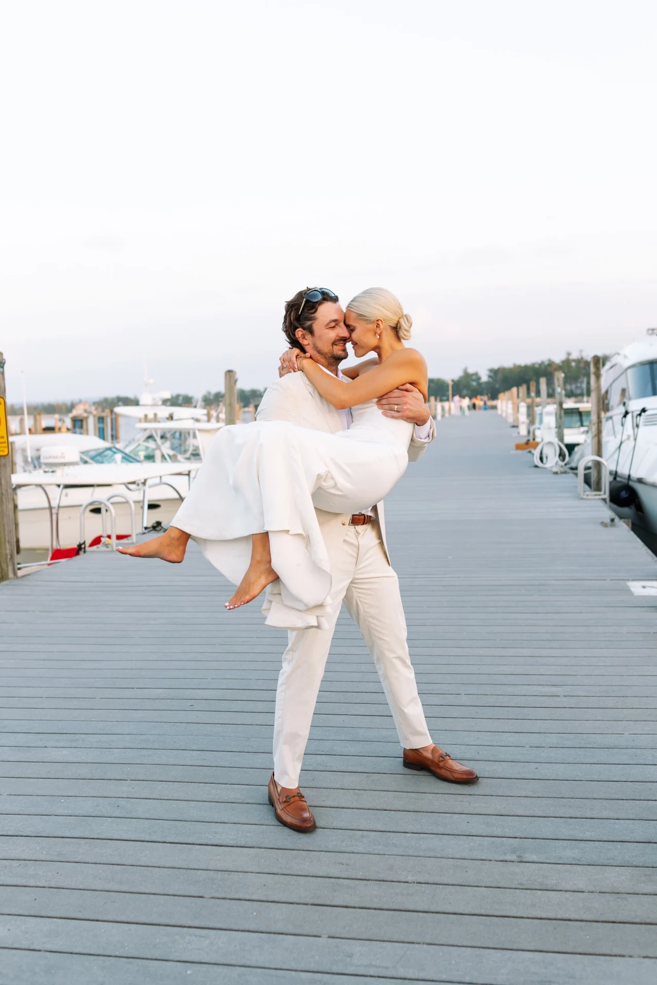 Groom lifting his bride in his arms on the marina dock at sunset