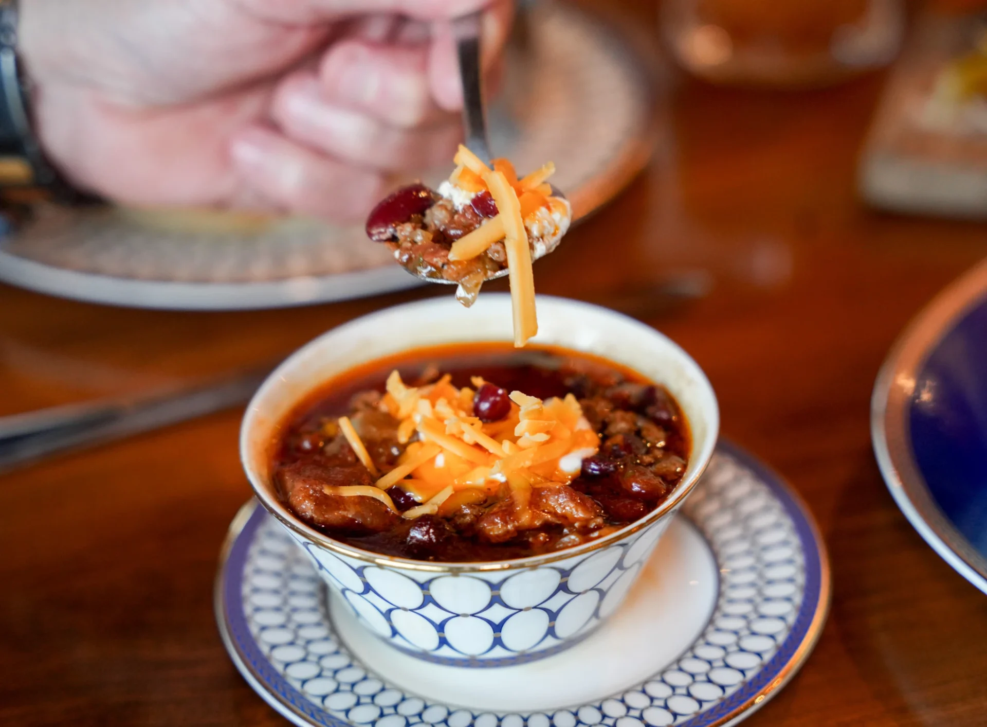 Spoonful of chili topped with shredded cheddar lifted from a china bowl