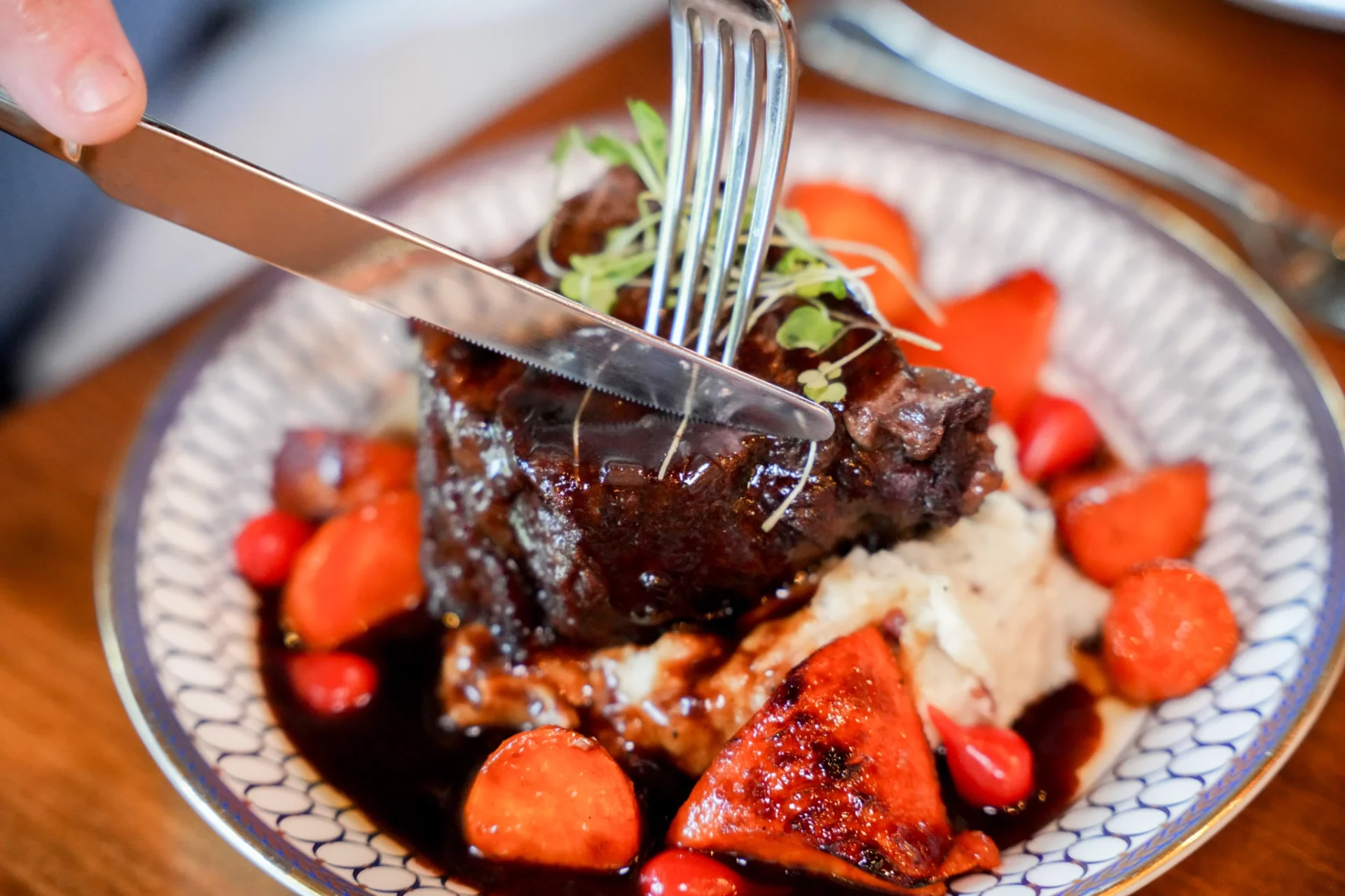 Fork and knife cutting into braised short rib with roasted carrots